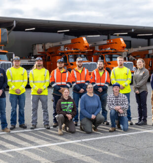 a group of electrical apprentices and trainees in front of large orange work trucks