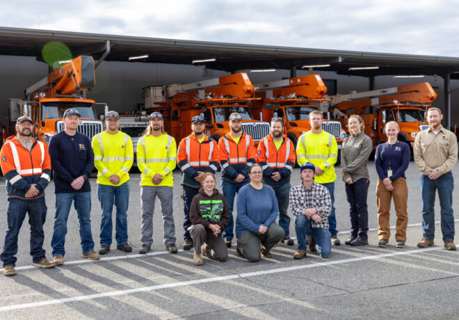 a group of electrical apprentices and trainees in front of large orange work trucks