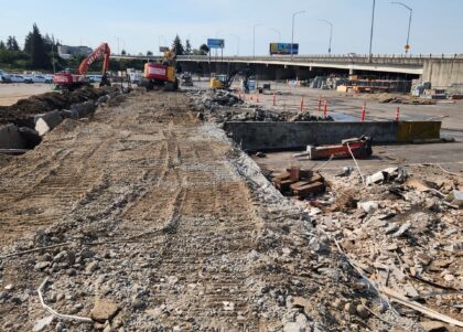 Demolition equipment and rubble fill a former loading-dock area beneath an elevated roadway.