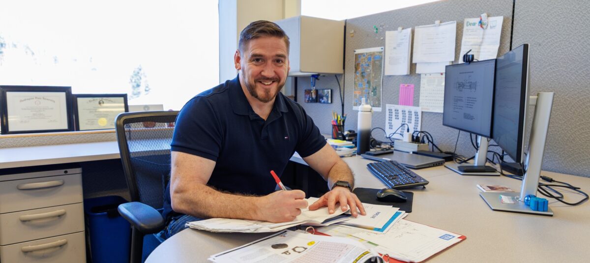 A man sits at a desk with pen in hand and paper on the desk. 