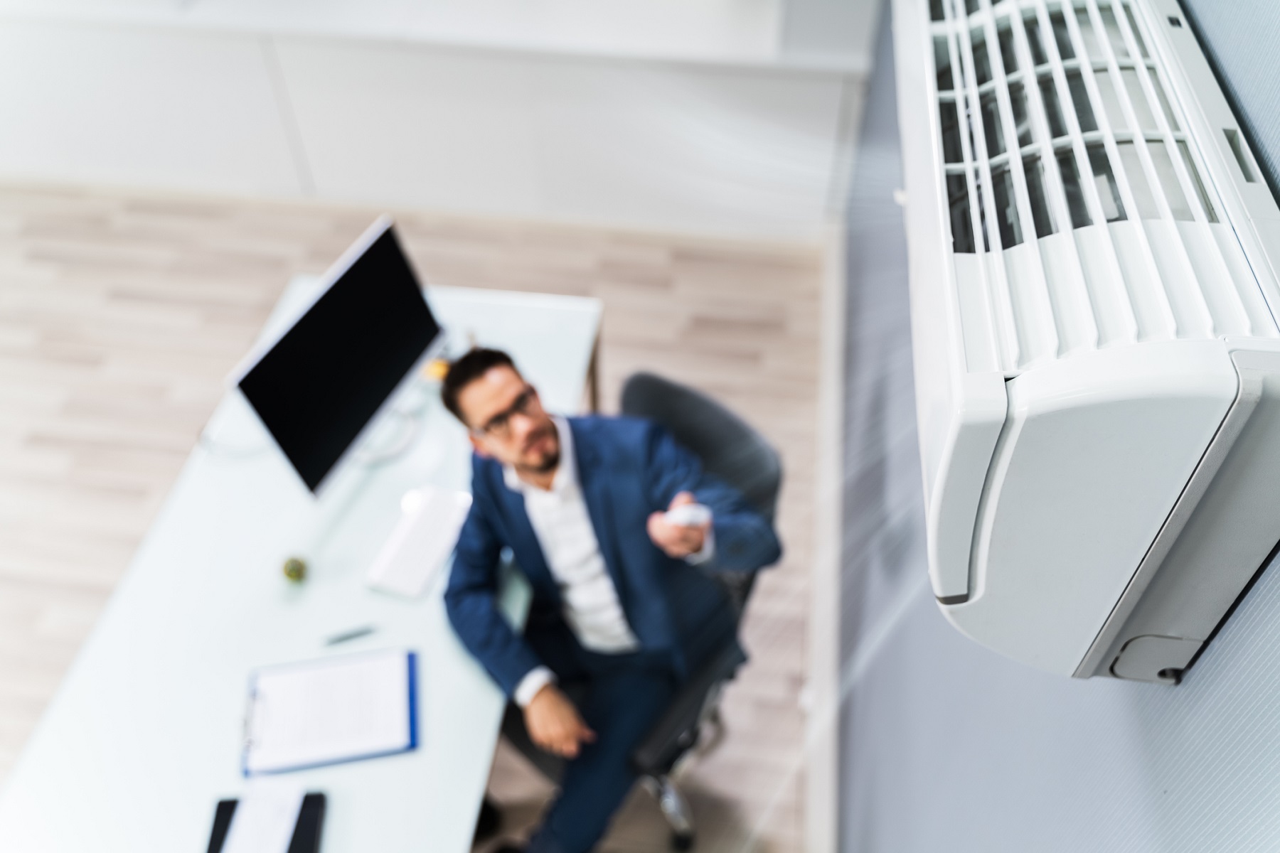 Image of a Business person Using Remote Control In Front Of an HVAC unit Mounted On Wall