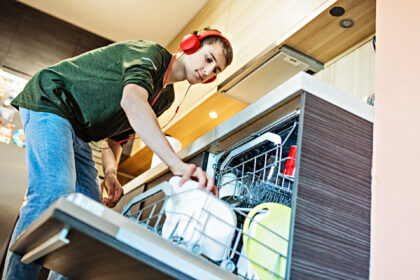 teenager wearing headphones, helping in the kitchen, loading the dishwasher