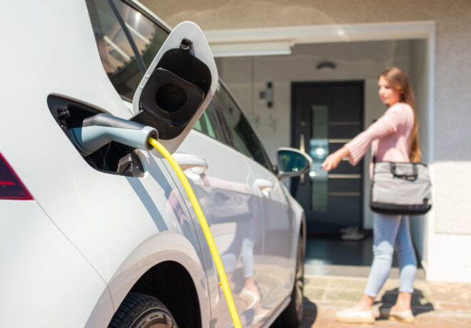 Electric vehicle parked at a home charging station with a cable plugged into the car, charging in a residential driveway.
