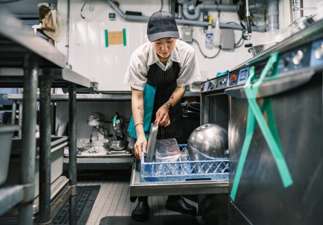 a person loading a commercial kitchen dishwasher