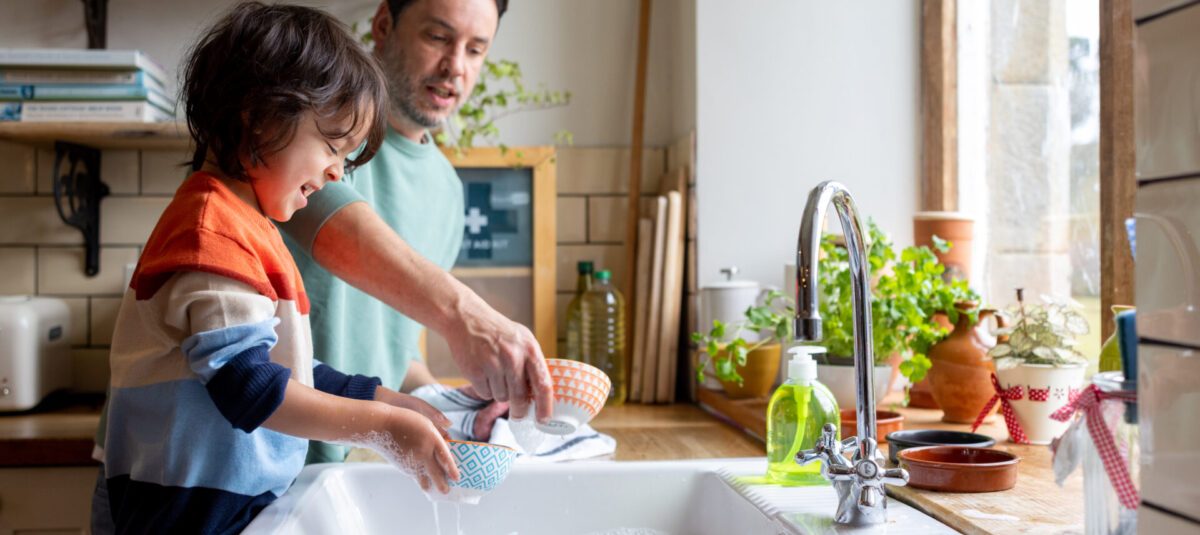 Adult and child wash patterned bowls together at a kitchen sink.