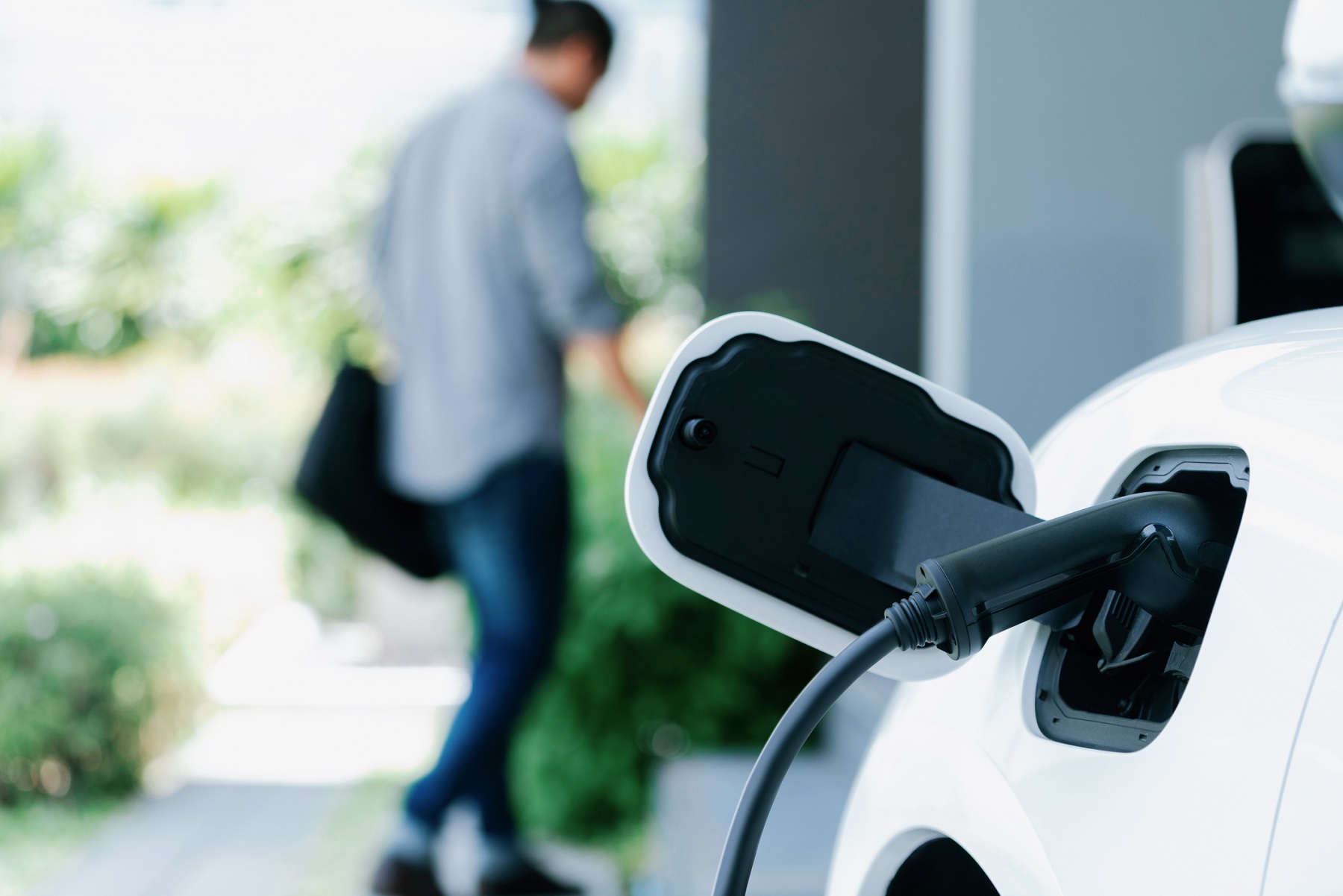 electric car charging at home charging station with blurred progressive man walking in the background.