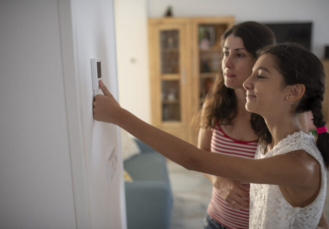 Woman and daughter adjust temperature of their home using a wall-mounted touch pad thermostat.