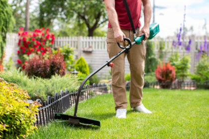 A man cutting the lawn with cordless grass trimmer, edger, using modern garden equipment at private backyard.
