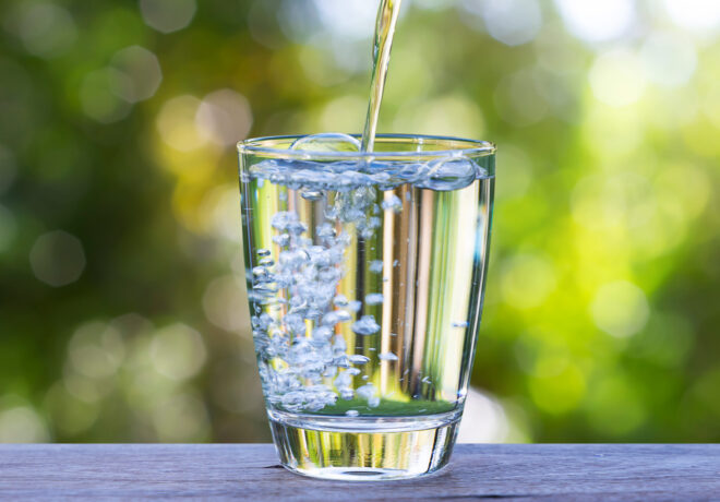 Pouring drinking water into glass on wooden table on blurred green nature background