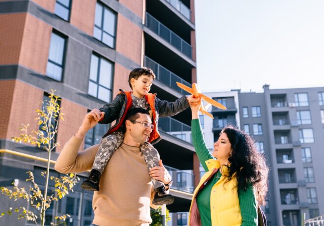A family walks together through a landscaped apartment community on a sunny day. Modern multifamily housing, trees, and pedestrian pathways create a welcoming neighborhood setting that reflects community, comfort, and quality of life.