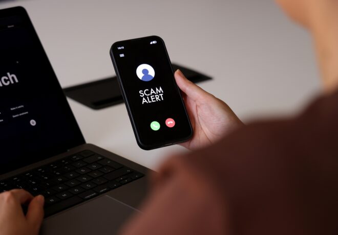 A person holds a smartphone displaying a “Scam Alert” message on an incoming call screen. The dark interface clearly indicates a fraud warning, conveying concerns about cybersecurity, mobile fraud, and digital safety. The indoor environment and close-up composition highlight the immediacy and relevance of online threat awareness in everyday mobile use.