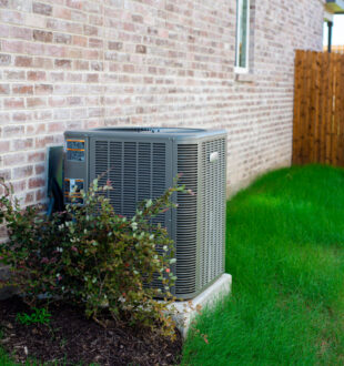An Outdoor HVAC unit and wall mounted electrical boxes installed alongside modern brick home,