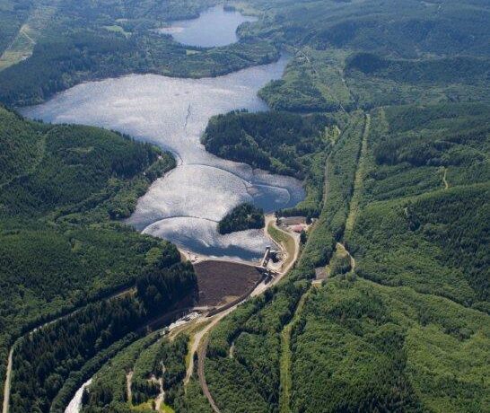 Aerial view of the Howard Hanson Dam on the Green River, surrounded by green forests and mountains under a cloudy sky.