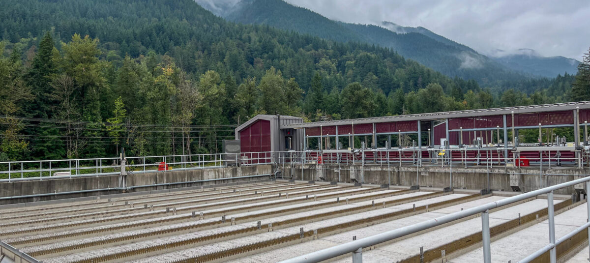 Water filtration facility with concrete treatment basins and industrial equipment set against a misty, forested mountain landscape.
