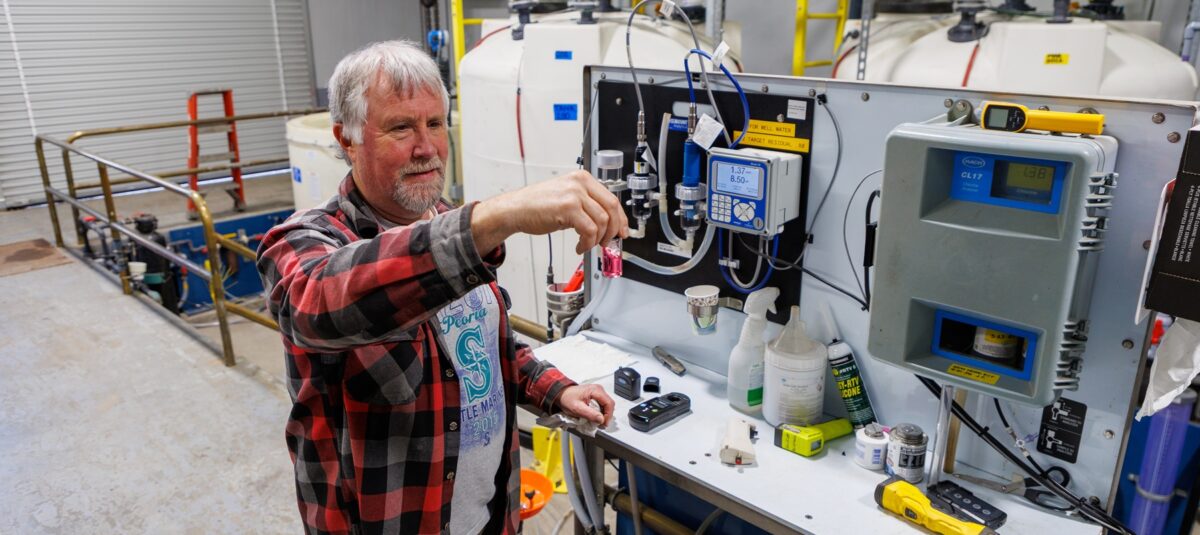 A man examines at a vial of water while standing in front of a water analysis machine.