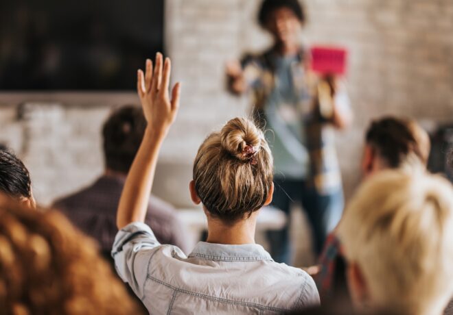 Rear view of casual businesswoman raising her hand to ask the question on education event in a board room.