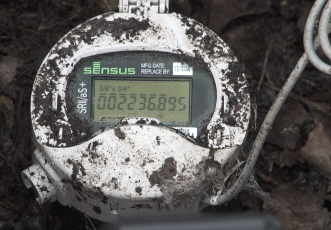 Close-up of a mud-covered Sensus water meter displaying approximately 002236895.