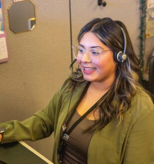 Female TPU customer service representative talking to a customer on a phone headset sits at a computer similing.