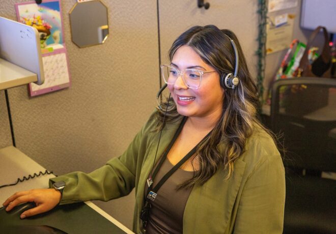 Female TPU customer service representative talking to a customer on a phone headset sits at a computer similing.