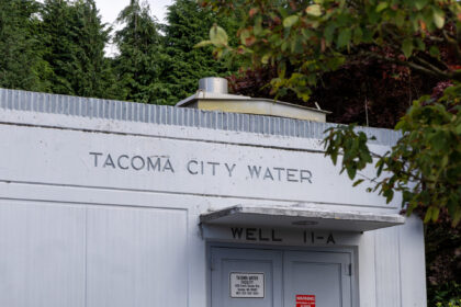 The single-story gray concrete South Tacoma Way Well Station-3 well building surrounded by trees.