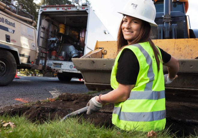 Female water utility employee looking at the camera while digging a hole.