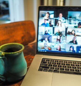 Laptop sitting on a table next to a mug. The computer screen shows people atteneding a virtual meeting.