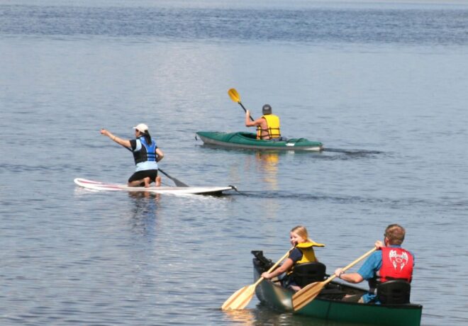 Three people paddleboarding on the lake in life jackets.