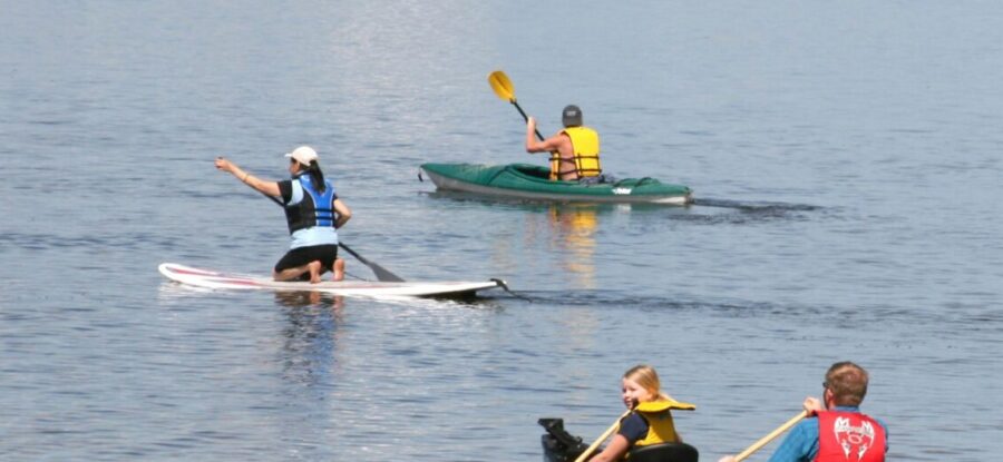 Three people paddleboarding on the lake in life jackets.