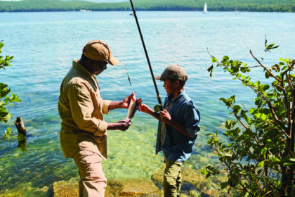 Side view of happy mature black man in activewear showing fish to his grandson
