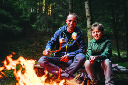 Father and son roast marshmallow candies on the campfire in forest