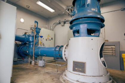 Industrial groundwater well pump room with large blue pipes and a white cylindrical pump housing.