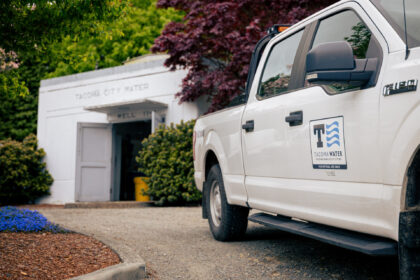 White Tacoma Water utility truck parked in front of a building labeled “Tacoma City Water” and “Well 11.”