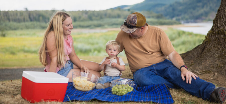 family eating a picnic with a red cooler, grapes, and nature in the background