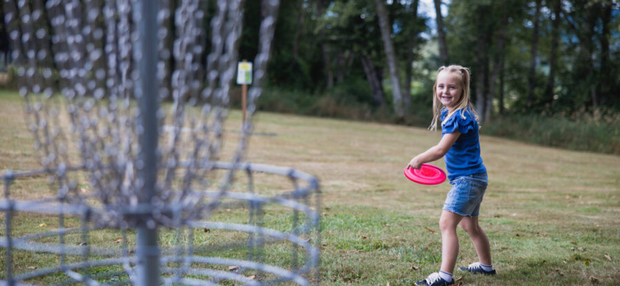 young girl in blue shirt throwing a frisbee in disc golf