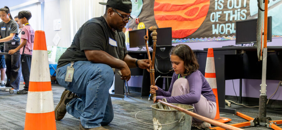 a TPU water utility worker showing a female identifying child how to connect a water pipe